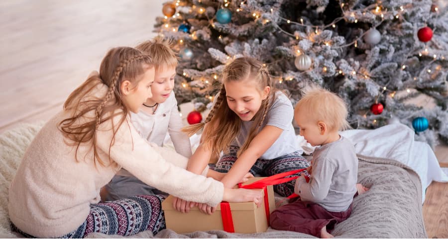 Kids opening a present in the family room near a Christmas tree.